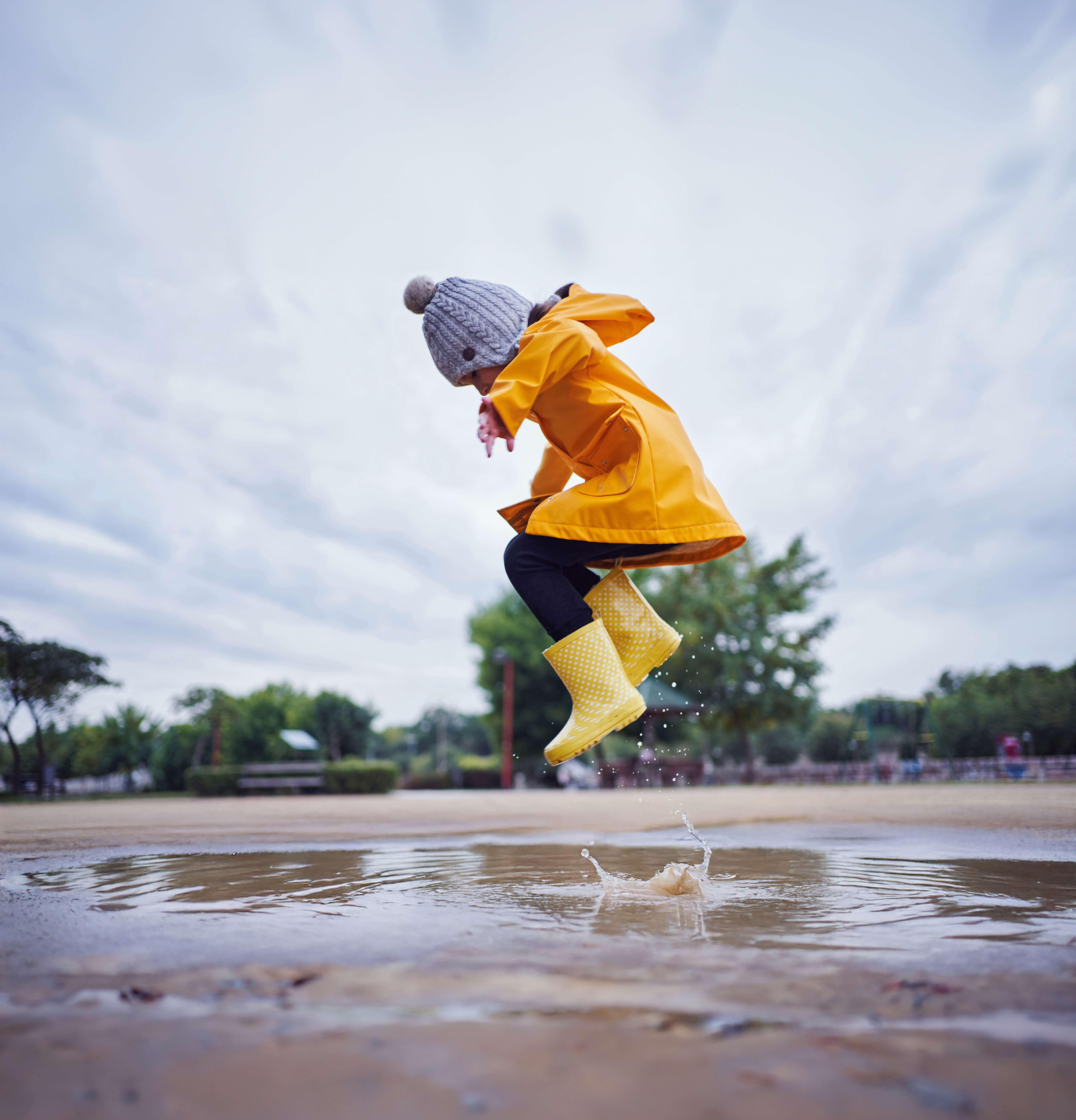 Meisje springt in een plas met gele regenlaarzen