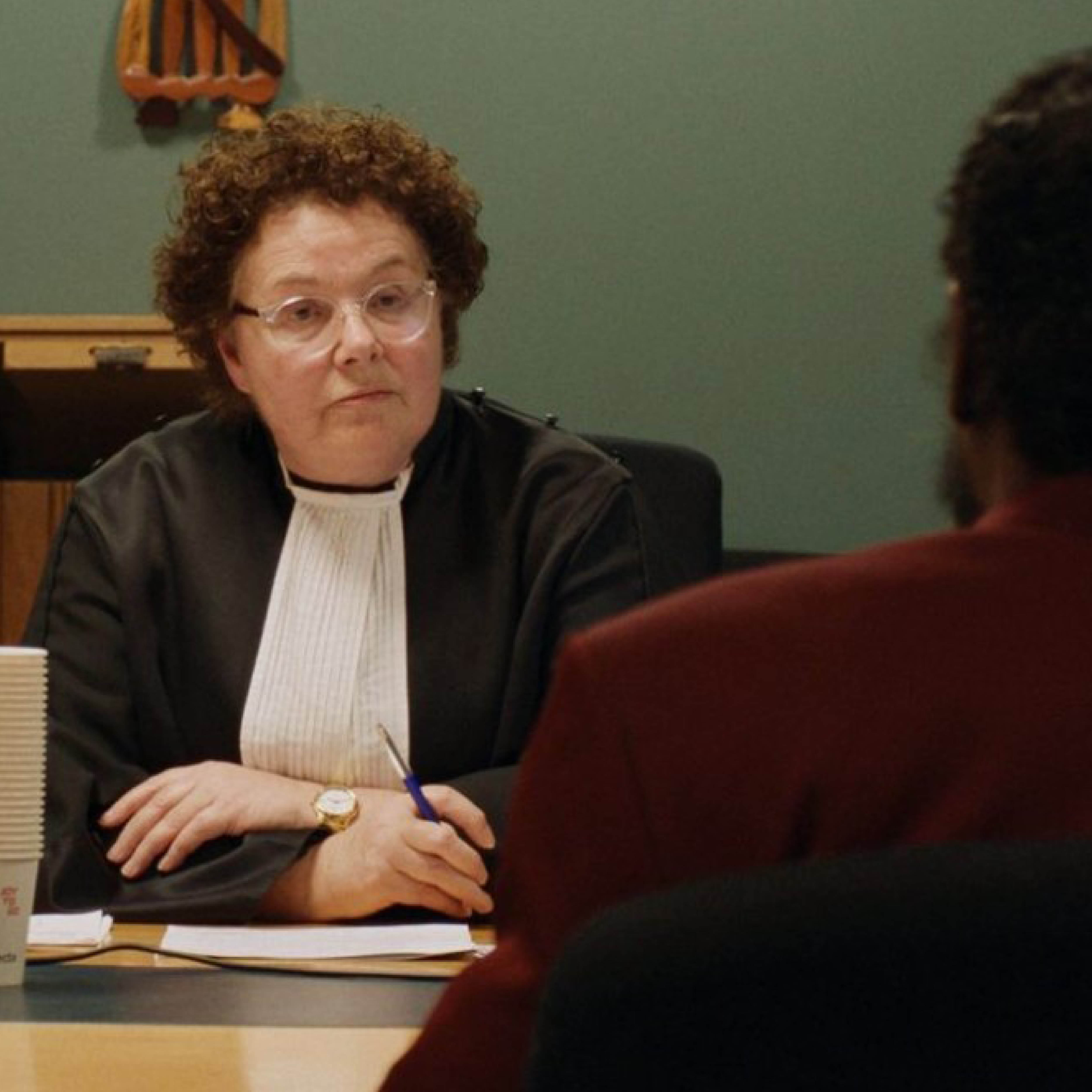 Een vrouwelijke rechter zit achter een tafel.