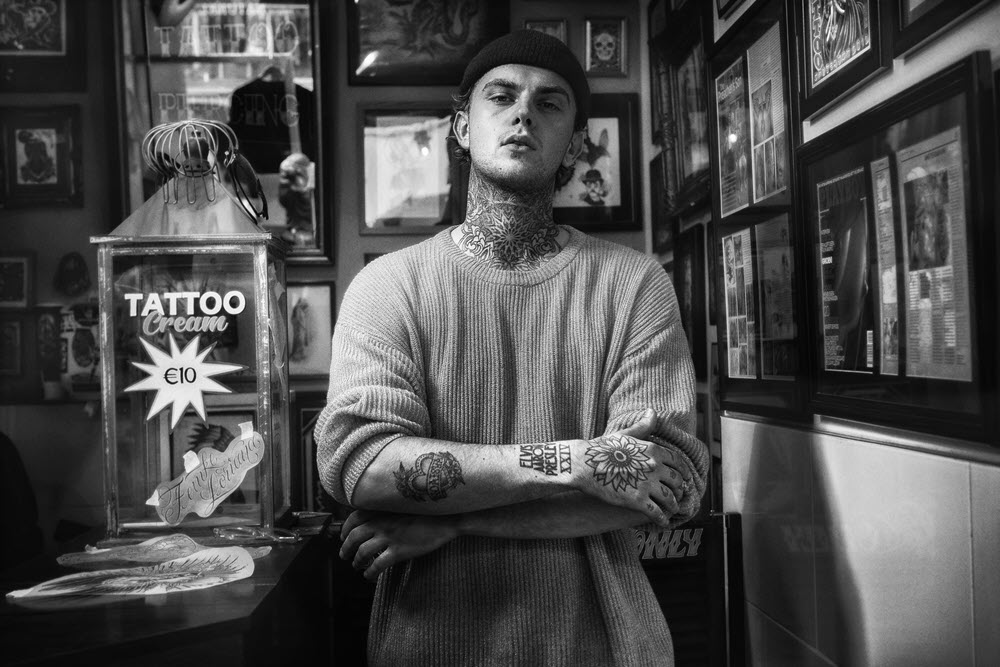 Jongeman met muts op staat in zijn tattoo shop.