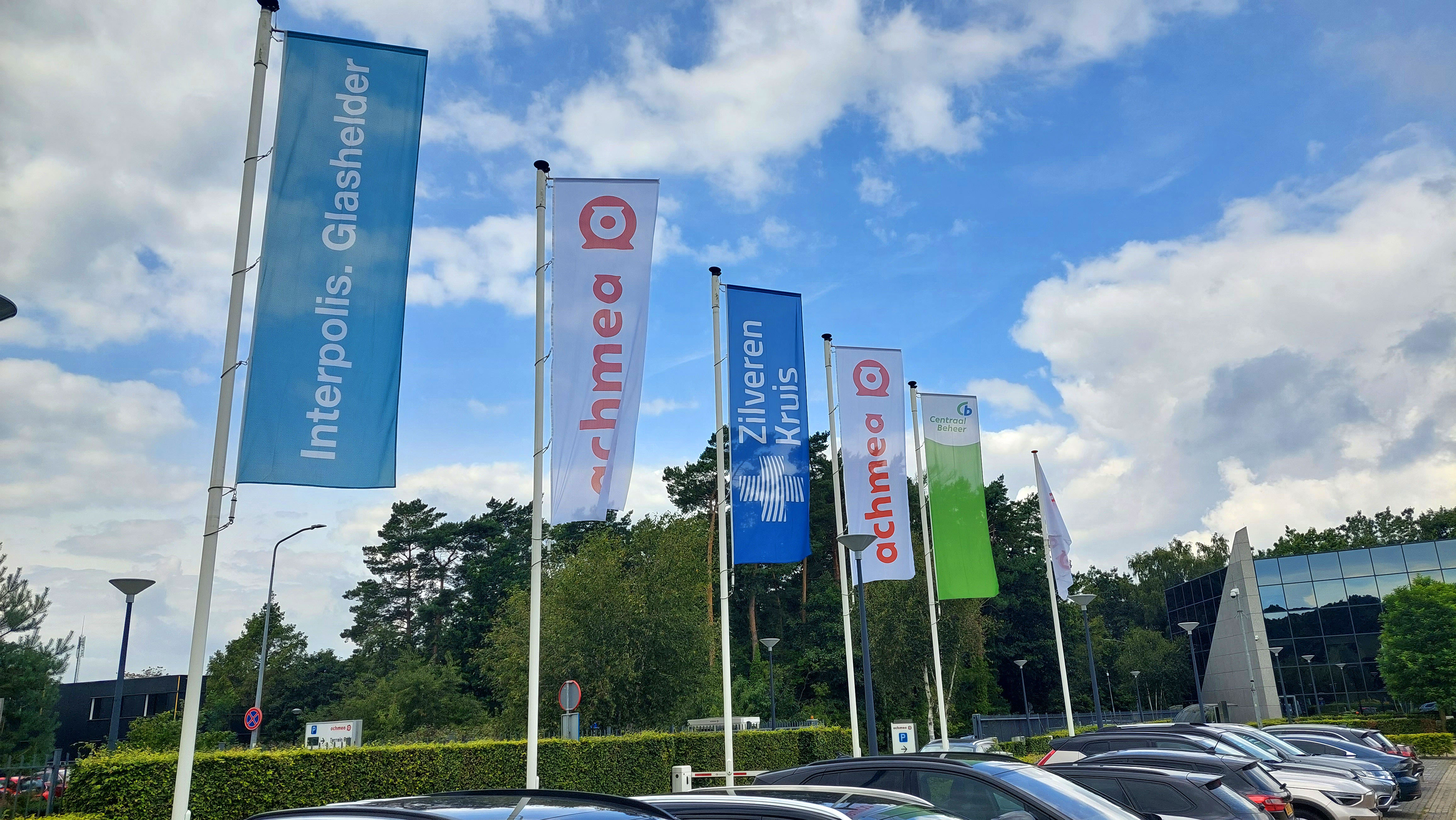 Rijtje vlaggen met logo's van Achmea's merken op het parkeerterrein bij het kantoor in Zeist