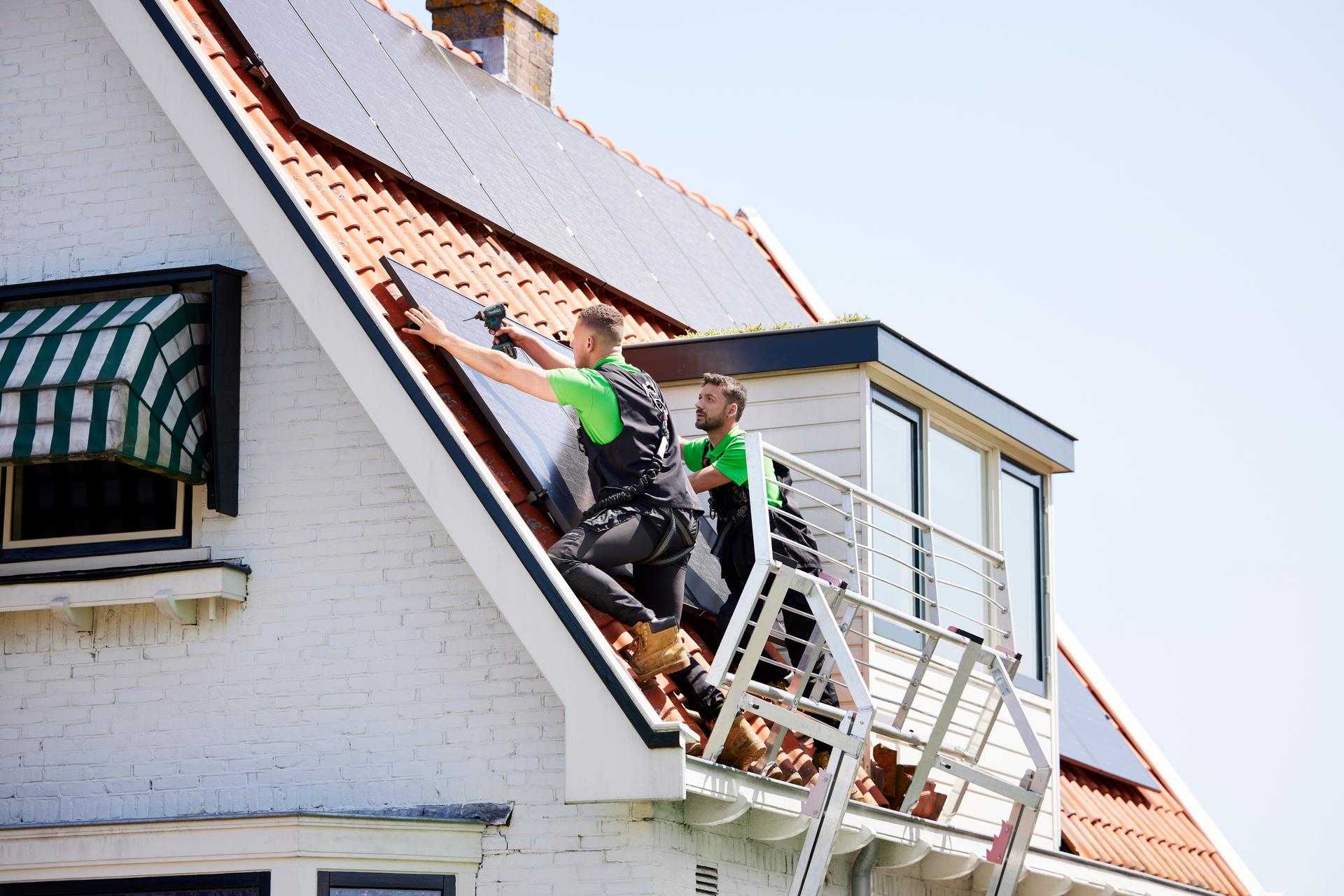Installateurs van zonnepanelen installeren een zonnepaneel op het dak van een huis