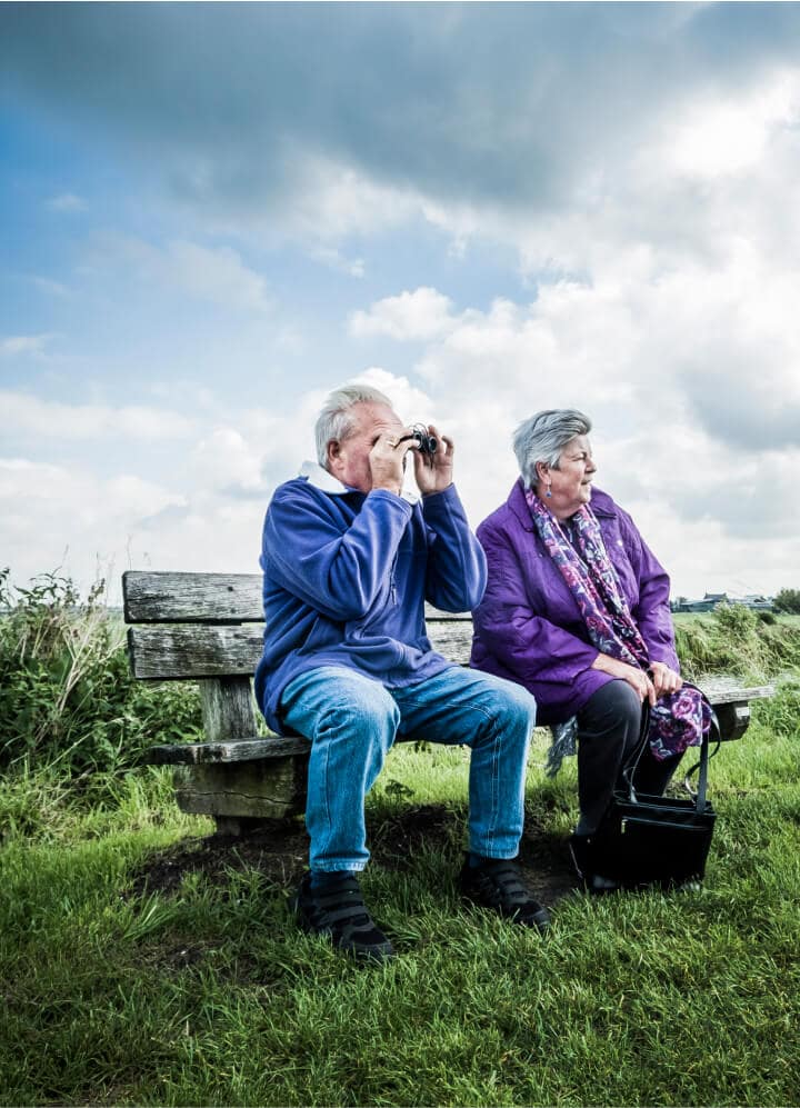 2 ouderen op bankje buiten, kijkend door een verrekijker