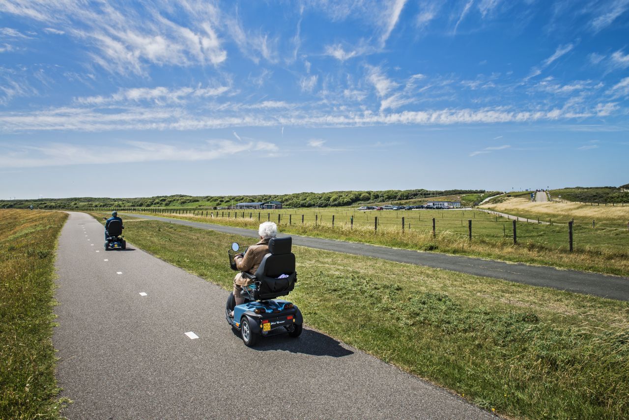 Een oudere vrouw op haar scootmobiel op een fietspad in de duinen