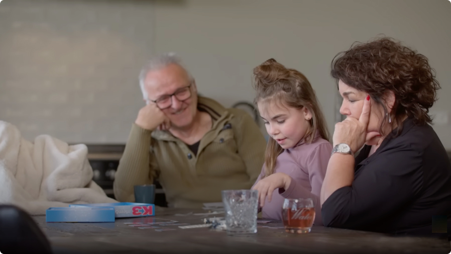 Een familie (opa, moeder en dochter) speelt een spelletje aan tafel 