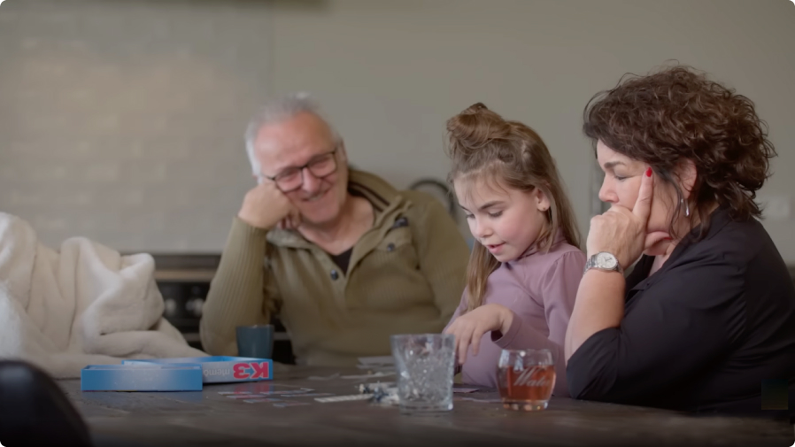 Een familie (opa, moeder en dochter) speelt een spelletje aan tafel