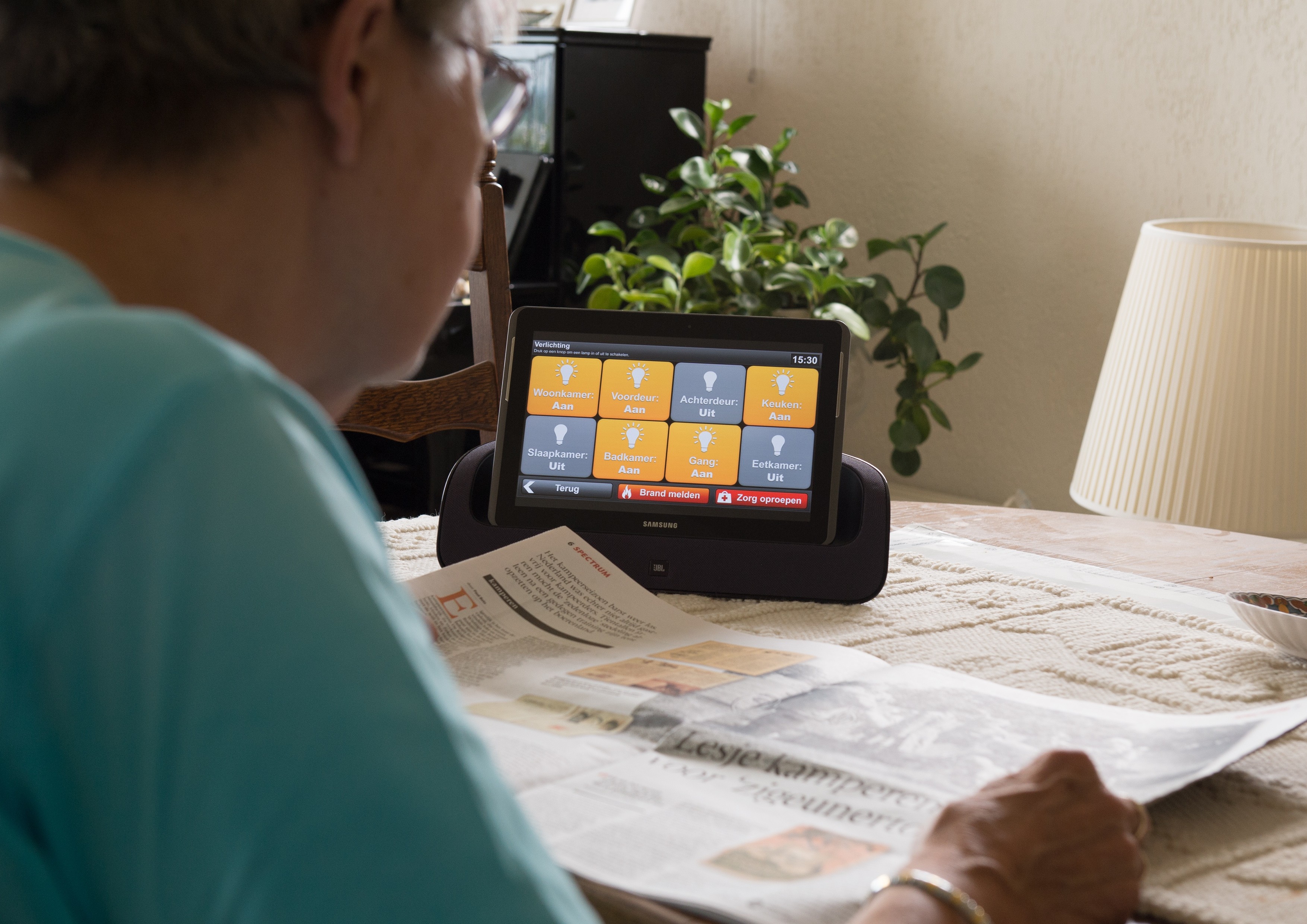 Oudere dame leest de krant en heeft een tablet als hulpmiddel