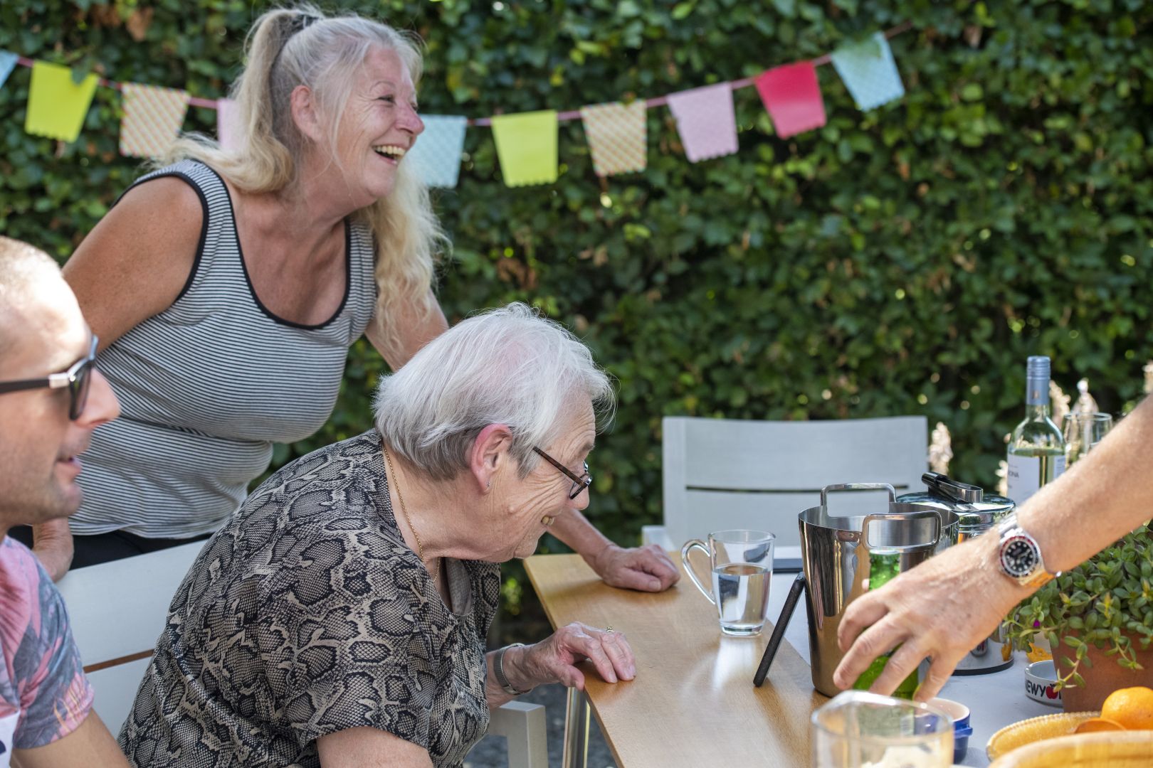 Een oudere vrouw viert feest in de tuin, omringd door geliefden en slingers