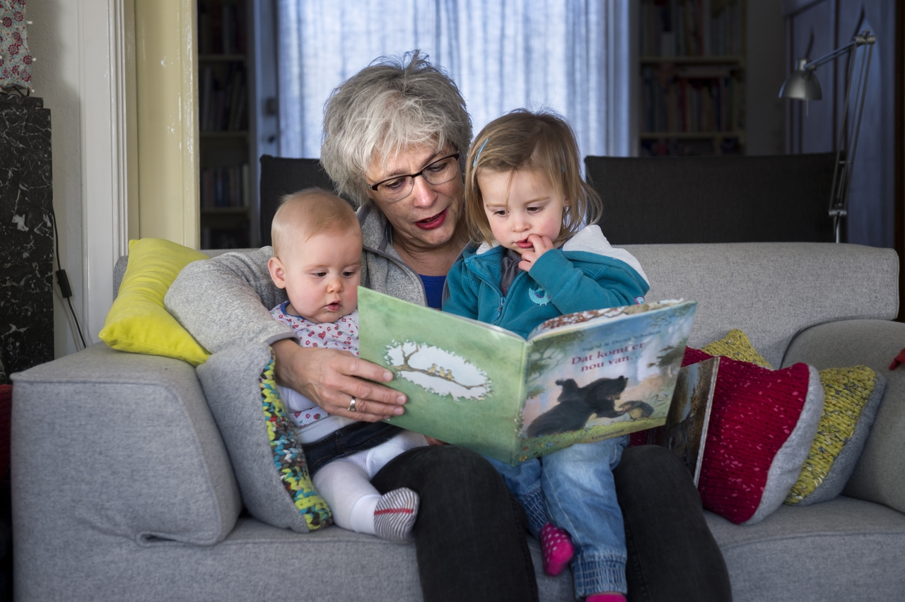 Oma zit op de bank en leest twee kleinkinderen voor die bij haar op schoot zitten