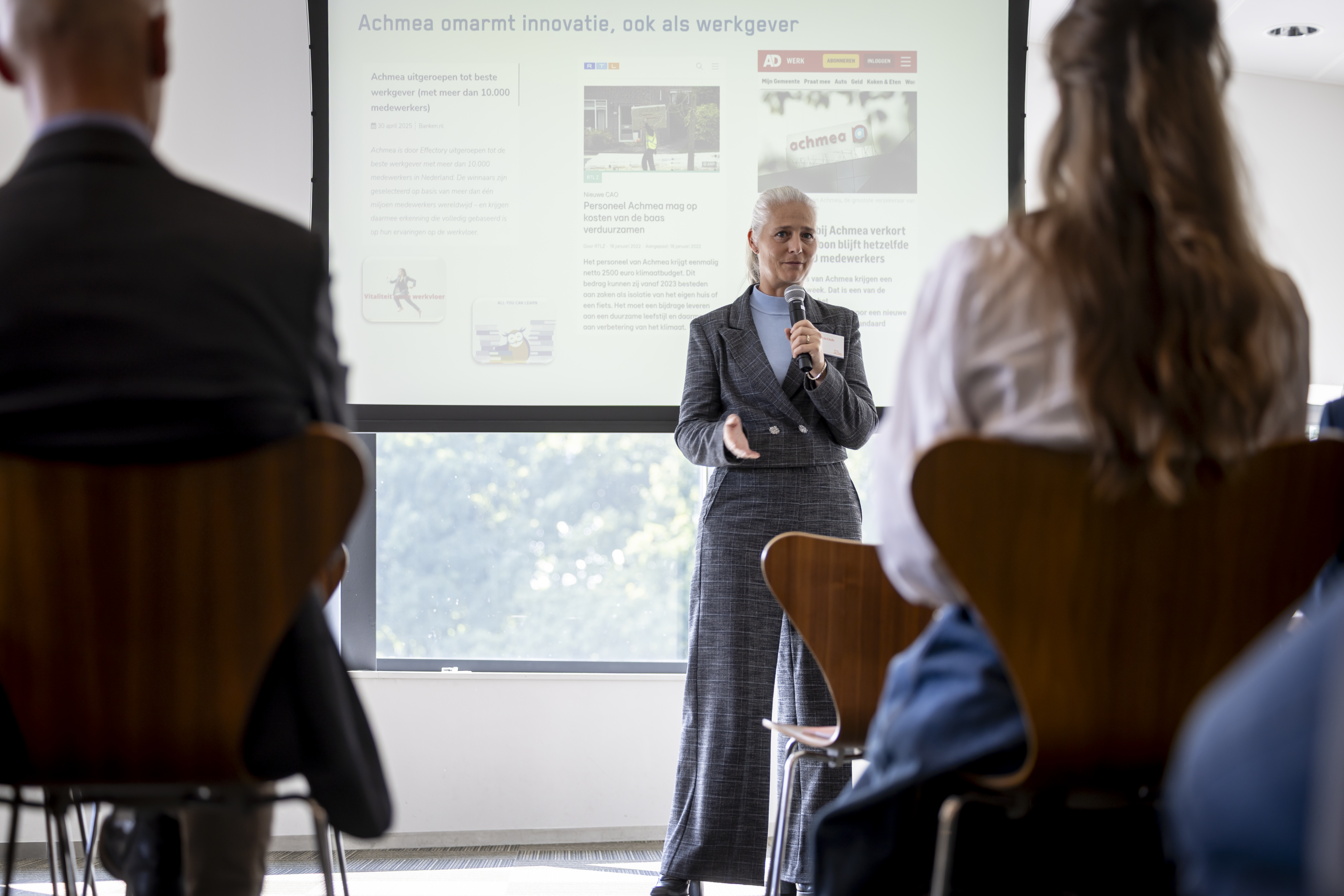 Patricia Gielis presenteert tijdens Over de Vloer XL over Duurzaam Werkgeverschap bij Achmea. Ze staat met een microfoon voor de slide Slide Achmea omarmt innovatie, ook als werkgever