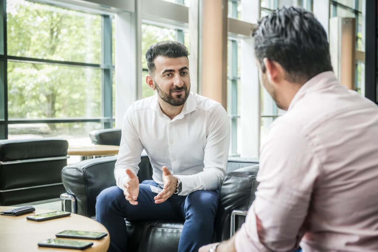 Twee mannen zitten en zijn in gesprek met telefoons op tafel