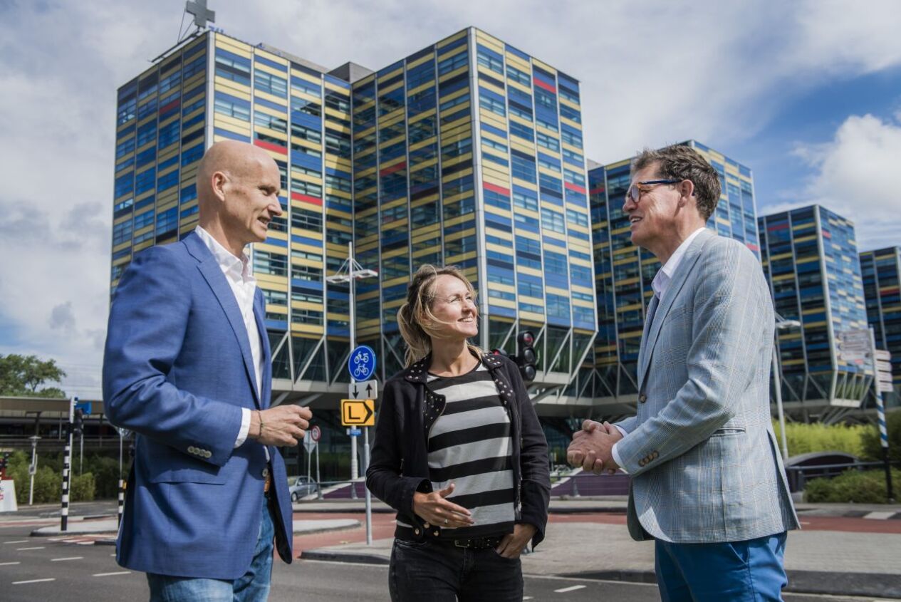 Twee mannen en een vrouw staan buiten een kantoorpand te overleggen