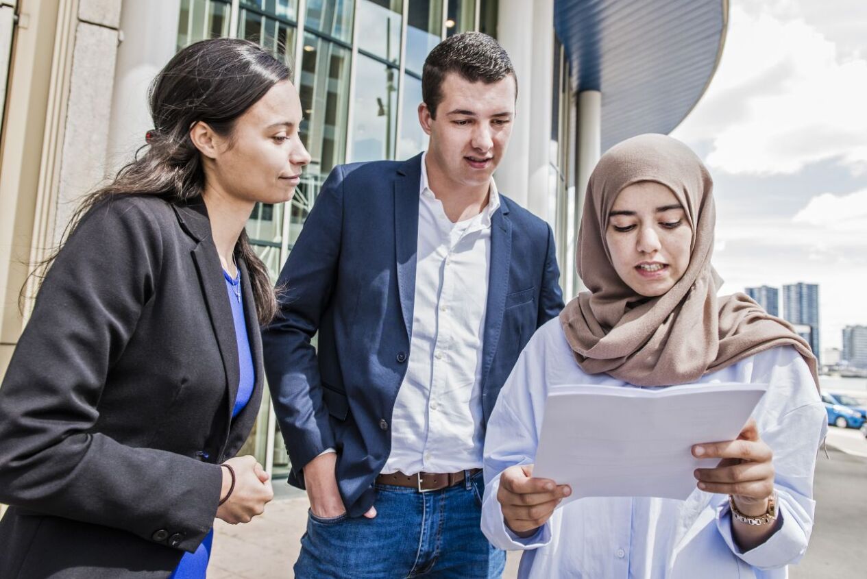 Een vrouw houdt papieren vast, ze praat en een andere vrouw en man kijken mee